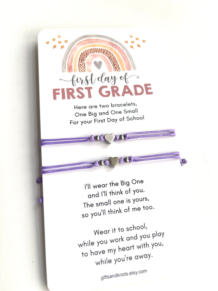 First day of FIRST GRADE card is accompanied by two purple friendship bracelets with silver heart charms. The text on the card reads 'Here are two bracelets, One Big and One Small For your First Day of School. I'll wear the Big One and I'll think of you. The small one is yours, so you'll think of me too. Wear it to school, while you work and you play to have my heart with you, while you're away.